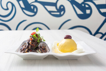 Black peel eviction, accompanied by huancaína potatoes, on a white plate.

