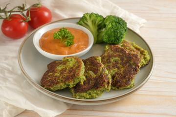 Vegetable patties of broccoli and flaked oats with tomato sauce, vegetarian and vegan meal on a plate and a light wooden table, selected focus