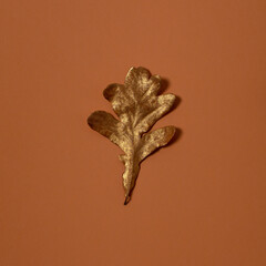 Gold autumn oak leaf on brown ocher background. Minimal season design. Creative composition.