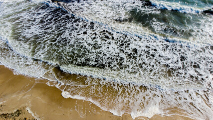 Fototapeta na wymiar Aerial drone view flight over sea waves that roll onto sandy shore.