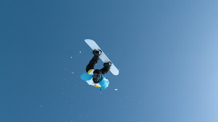 Naklejka na ściany i meble Fearless male snowboarder does a backflip after jumping off a massive kicker.