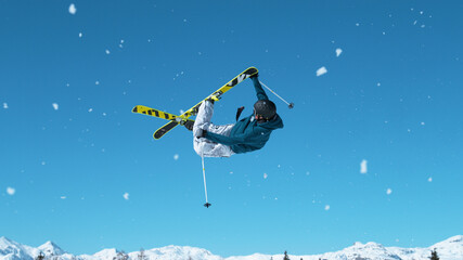 Athletic male skier jumps high into the air and performs an extreme grab trick.