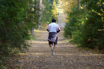 Athlete man running in autumn forest during cold foggy morning. Male jogger training outdoors before marathon in nature park jogging along trail. Fit sportsman exercising in october fall woods alone