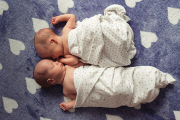 Portrait of sleeping newborn twins. Twin girls wrapped in diaper with free hands. Selective focus. Film grain