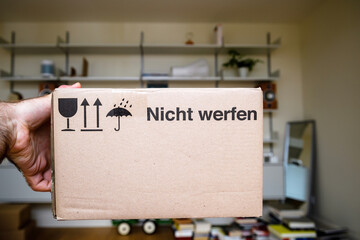 POV male hand holding package cardboard box with text in German Nicht werfen translated as do not...