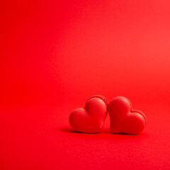 Two red heart shaped French macaron cookies on a bright red backdrop 