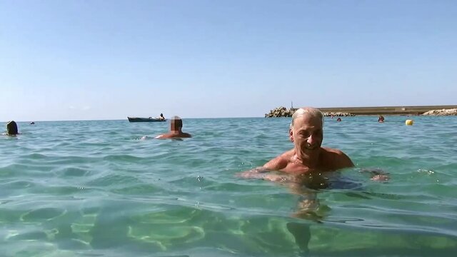 Caucasian elderly man swimming in the sea. Beach.