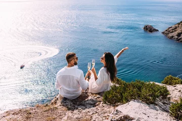  A couple in love celebrates their engagement on the seashore. A beautiful couple drinks champagne by the sea. Honeymoon trip. Lovers on the beach. Wedding travel. Couple on vacation. Copy space © MISHA