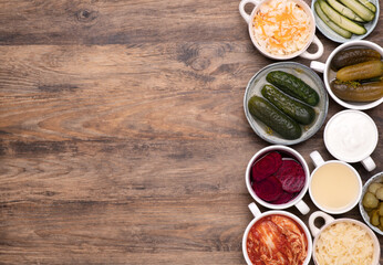 Healthy probiotic fermented foods in cups and bowls on wooden table, top view with copy space