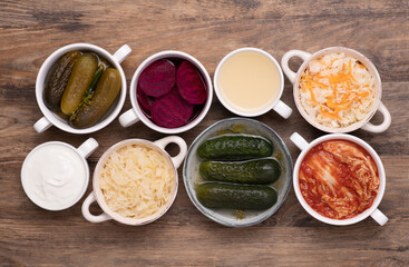 Healthy probiotic fermented foods in cups and bowls on wooden table, top view 