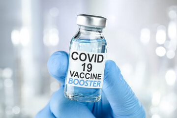 Hand in blue medical gloves holding a vaccine vial with Covid 19 Vaccine Booster text, for Coronavirus booster shot. - obrazy, fototapety, plakaty