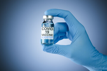 Hand in blue medical gloves holding a vaccine vial with Covid 19 Vaccine Booster text, for...