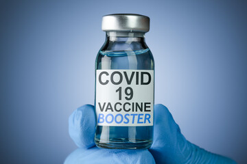 Hand in blue medical gloves holding a vaccine vial with Covid 19 Vaccine Booster text, for...
