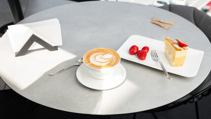 Classic cheesecake with fresh strawberry with cup of coffee on white table. Close Up view. Tasty breakfast. Piece of cake on plate, white cup on white marble background.