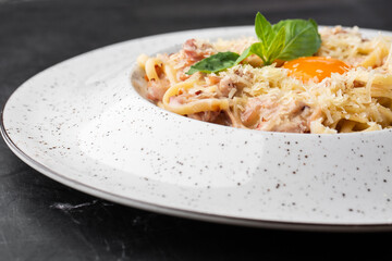 Pasta Carbonara. Spaghetti with bacon, parmesan, cream sauce and egg yolk. Macro close-up isolated on a white round plate. Mediterranean gourmet food.
