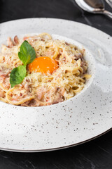 Pasta Carbonara. Spaghetti with bacon, parmesan, cream sauce and egg yolk. Macro close-up isolated on a white round plate. Mediterranean gourmet food.
