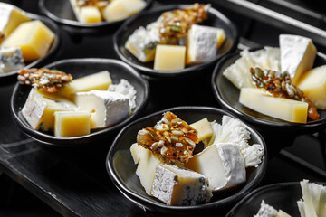 Diced cheese and nuts with honey in cups on a dark background.