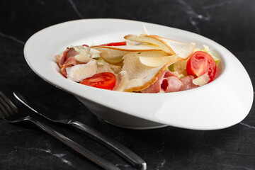 Caesar Salad. Grilled bacon, tomatoes, croutons, parmesan and fresh salad in plate. On black marble background.