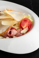 Caesar Salad. Grilled bacon, tomatoes, croutons, parmesan and fresh salad in plate. On black marble background.
