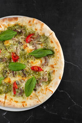 Delicious hot homemade pizza on black marble table. Pizza - Fresh homemade pizza with meat, cheese, tomato sauce, tomatoes, pumpkin seeds and basil.