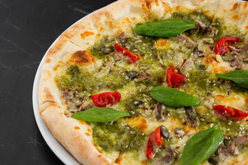 Delicious hot homemade pizza on black marble table. Pizza - Fresh homemade pizza with meat, cheese, tomato sauce, tomatoes, pumpkin seeds and basil.
