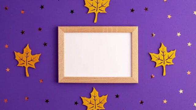 Stop motion animation of yellow felt autumn leaves star shapes and wooden picture frame on purple background with copy space. Halloween scary holiday and autumn concept