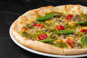Delicious hot homemade pizza on black marble table. Pizza - Fresh homemade pizza with meat, cheese, tomato sauce, tomatoes, pumpkin seeds and basil.