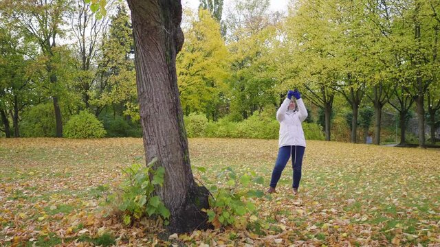 Asian woman taking a photo of view at park. Autumn outfits, Good weather, yellow leaves falling on the grass. A lot of tree background, Stockholm, Sweden in Autumn concept