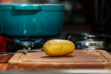 Raw potatoes on wooden board isolated. Defocused stove in the background with a pan.