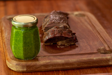 Grilled steak on a cutting board. Piece of filet mignon cut on a cutting board. Jar with fresh pesto sauce on the table.