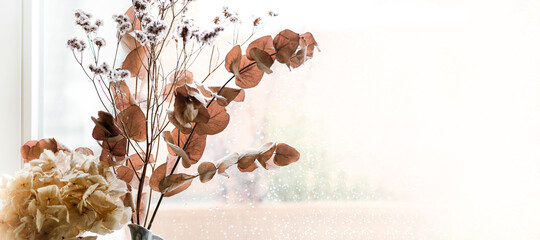 eine Blumendekoration aus getrockneten Pflanzen links un der Ecke vor einer Fensterscheibe - Blick durch das helle Fenster mit freier Fläche für Text