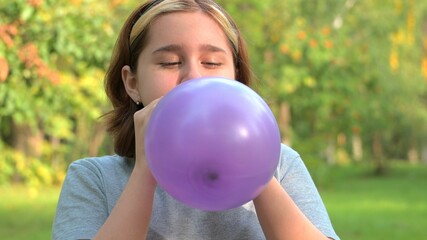 Naklejka premium a teenage girl inflates a lilac balloon close-up against the background of nature