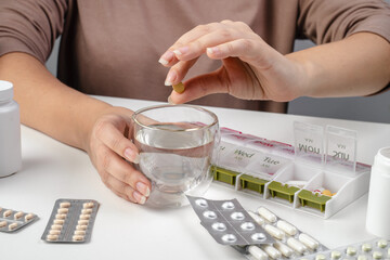 Hands of senior woman putting pills into pill box. Medicine container. Woman sorting drug pills for pain relief and disease treatment. Sick retired female with drugs. Daily vitamins for healthy