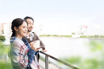 ベランダからコーヒーをもって外を見つめる日本人のカップル 横向き1 - obrazy, fototapety, plakaty