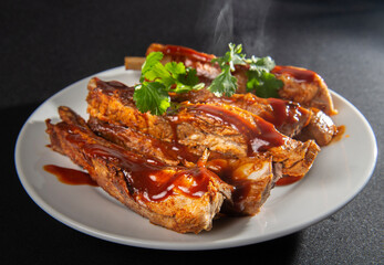 Steaming pork ribs with barbecue on a white plate and black background and a rim light and cilantro on top