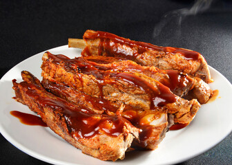 Steaming pork ribs with barbecue on a white plate and black background and a rim light Macro still life food photography
