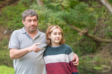 a teenage girl with a short haircut in a warm sweater with her dad in nature against the background of green nature in early autumn