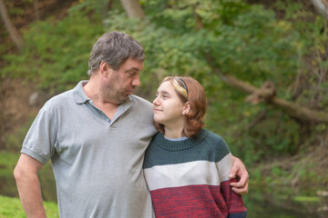 a teenage girl with her dad in nature look into each other's eyes against the background of green nature in early autumn