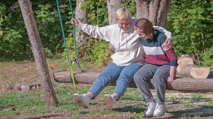 Naklejka na ściany i meble a teenage girl and her mom ride on a long wooden swing in nature