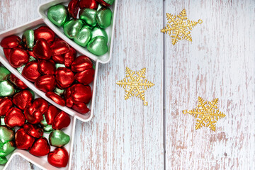 Heart shape chocolate candies and gold Christmas ornaments on a white pine shape plate.