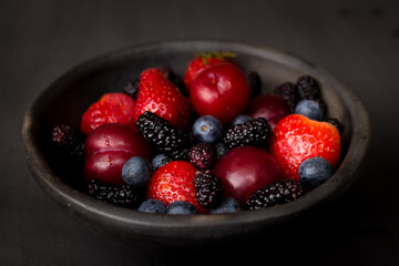 plate of fresh plums, blackberries, strawberries, blueberries on dark background