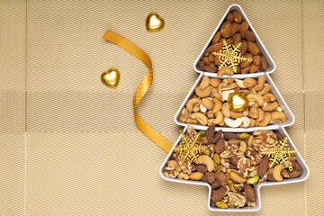 Mixed nuts and gold Christmas ornaments in a pine shape plate.