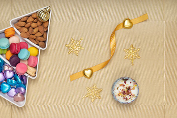 Mini macaroons and chocolate candies with Christmas ornaments on metallic gold background.