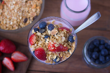 glass with yogurt, cereals, strawberries and blueberries on wooden table -  topview closeup