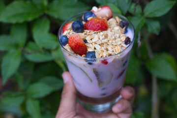 hand with glass with yogurt, cereals, strawberries and blueberries - closeup