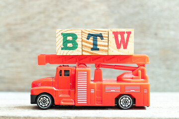 Fire ladder truck hold letter block in word BTW (Abbreviation of by the way) on wood background