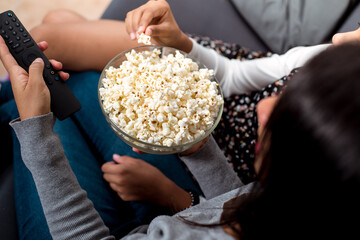 Photo seen from above of two girls sitting on the sofa, one of them is handling the remote control...