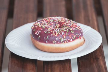 delicious donut on a white paper plate on a wooden table of a street cafe