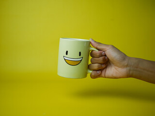 hand holding yellow coffee mug with smile emoticon icon. concept, happy and optimistic to start the day. morning spirit. Good morning