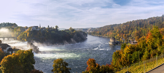 Panoramoa image of the Rhinefalls - the biggest waterfall in Europe - in the early morning with autumn fog and mist. The Laufen Castle stands on the hill top.